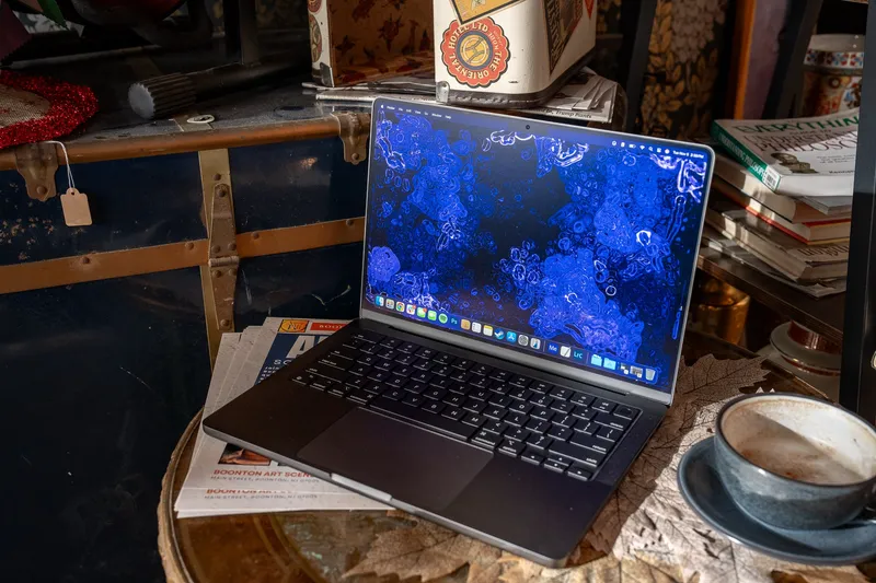 A 14-inch MacBook Pro M4 (2024) in space black sitting on an end table at a cafe with a coffee beside it.