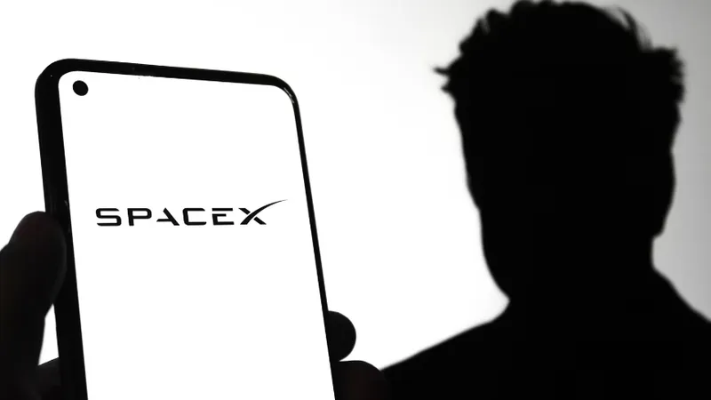 SpaceX logo on a mobile phone screen with SpaceX CEO Elon Musk silhouette in the background