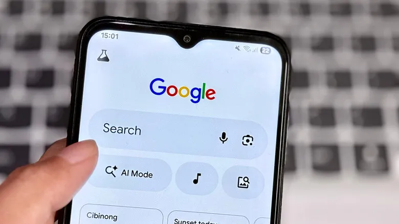 A hand holding a phone showing the Google home page.