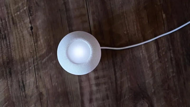 White spherical smart speaker with glowing center sits on a rustic wooden surface, connected by a single white power cable extending to the right