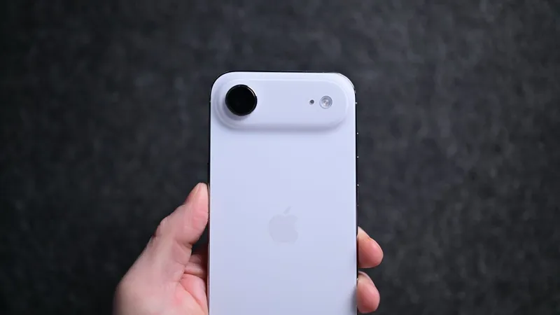 Hand holding a white iPhone seen from the back, featuring a large circular camera lens attachment on the top left against a dark, blurred background