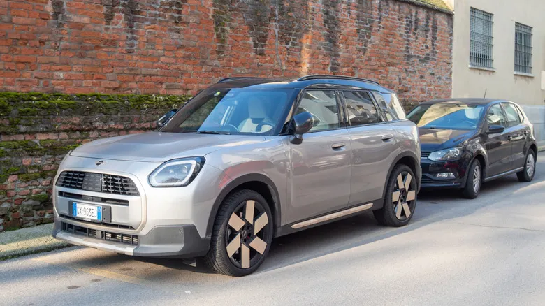A gray Mini Countryman SE ALL4 parked on the street in front of a brick wall